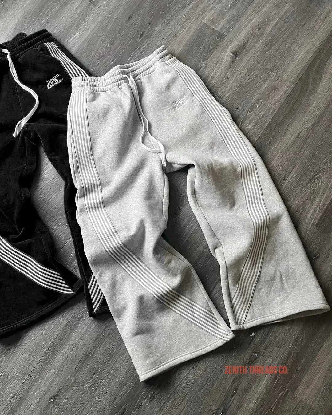 Athletic sweatpants with ribbed stripe detailing in light gray and black colors.