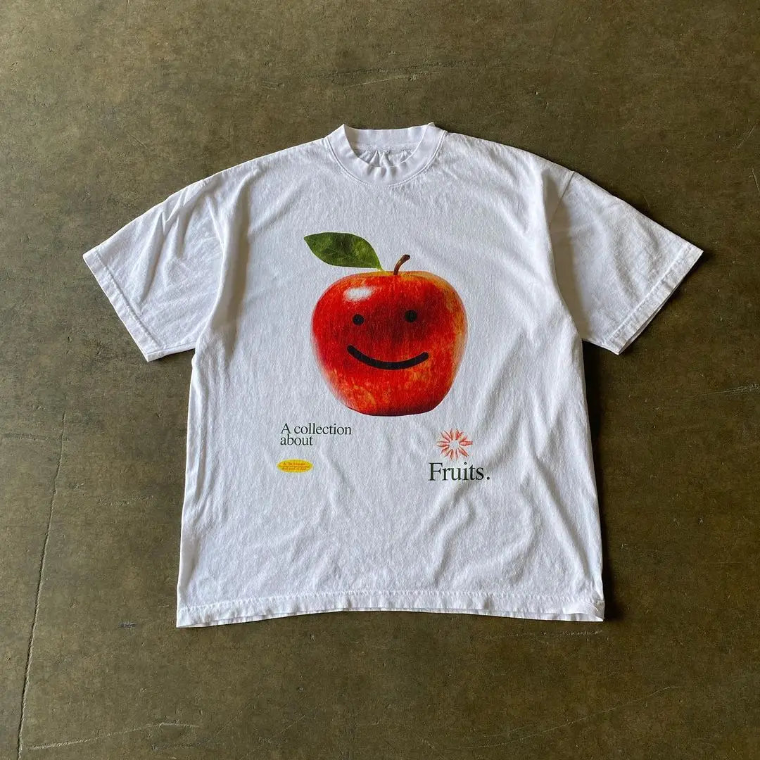 White t-shirt with a smiling red apple graphic printed on it.