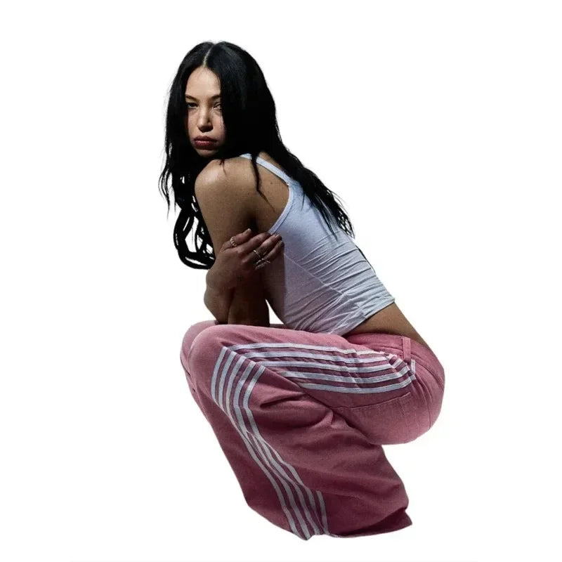 A dancer in a white tank top and pink striped track pants crouching in a dynamic pose.