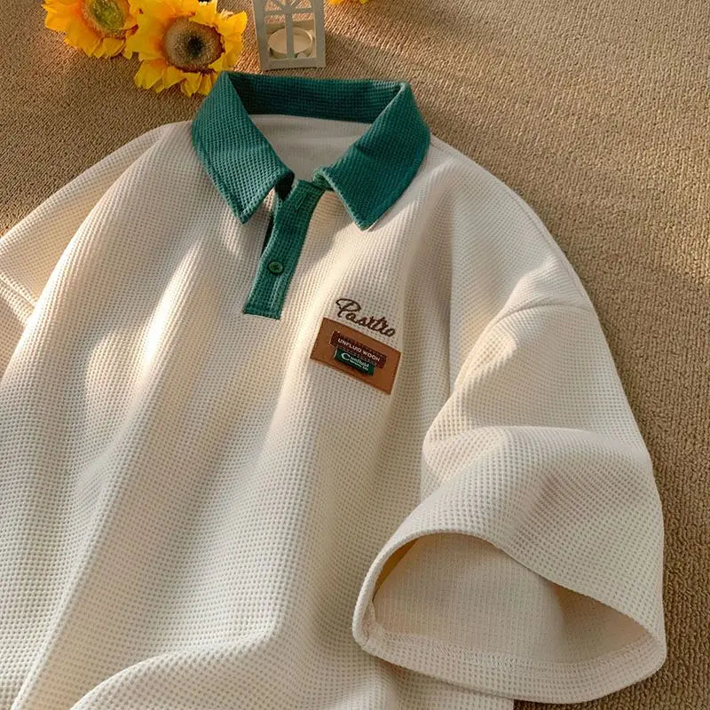 White polo shirt with a teal collar and a small patch emblem.