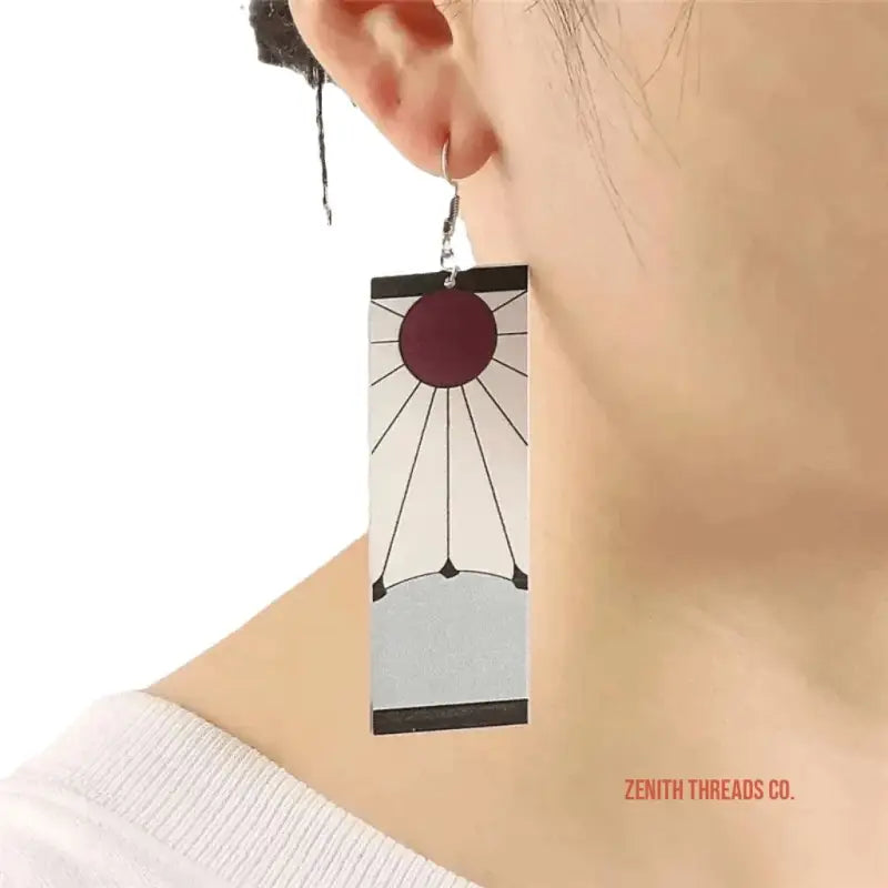 Geometric dangle earring featuring a burgundy circle with radiating black lines on a white rectangular base.