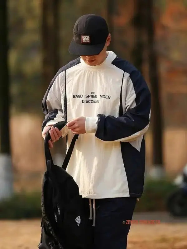 Someone wearing a white and navy blue color-blocked athletic jacket and baseball cap.