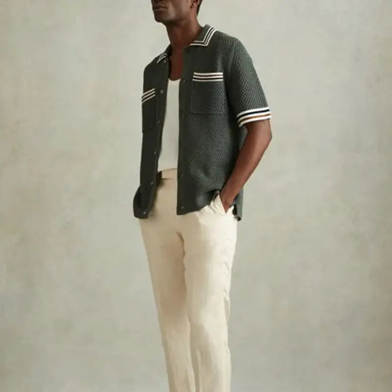 Dark green knit polo shirt with white striped trim worn with cream-colored pants.