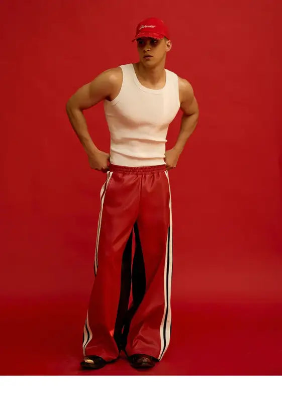 A person wearing a white tank top, red baseball cap, and red track pants with white stripes.