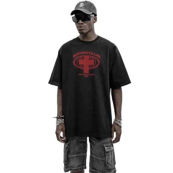 Man in black satan club graphic tee, denim shorts, and cap for bold fashion