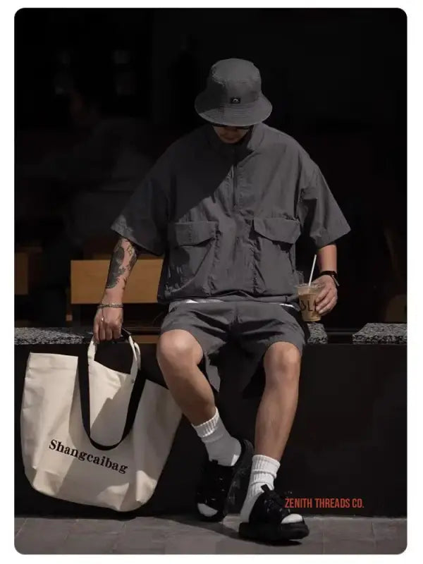 Person wearing a bucket hat, loose shirt, shorts and sneakers while holding a tote bag.