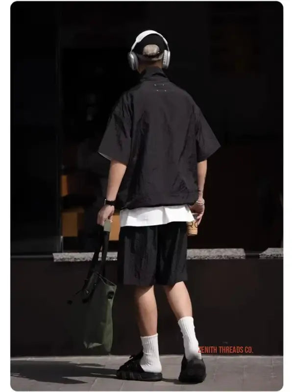 A skateboarder wearing headphones, a dark t-shirt, shorts and white socks.