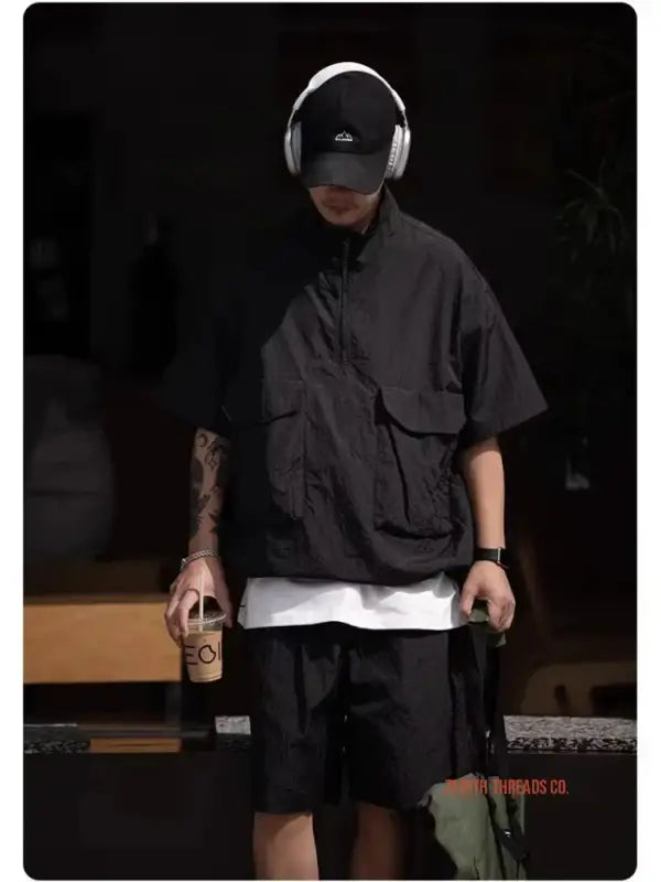 Someone wearing dark streetwear clothing with headphones and a baseball cap.