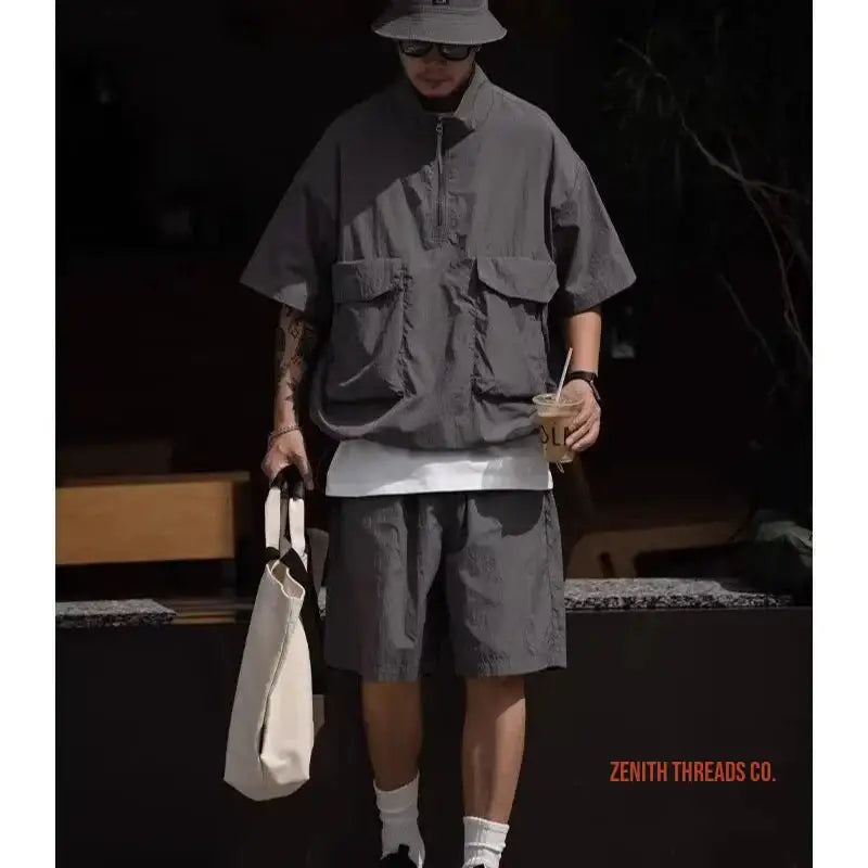 Person wearing a gray utility vest, matching shorts, bucket hat and carrying a white tote bag.