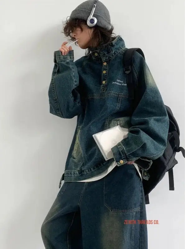 Oversized denim jumpsuit with decorative buttons and wide sleeves worn with white headphones.