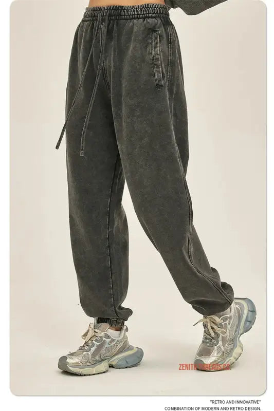 Dark gray sweatpants with drawstring waist and elastic cuffs worn with chunky gray sneakers.