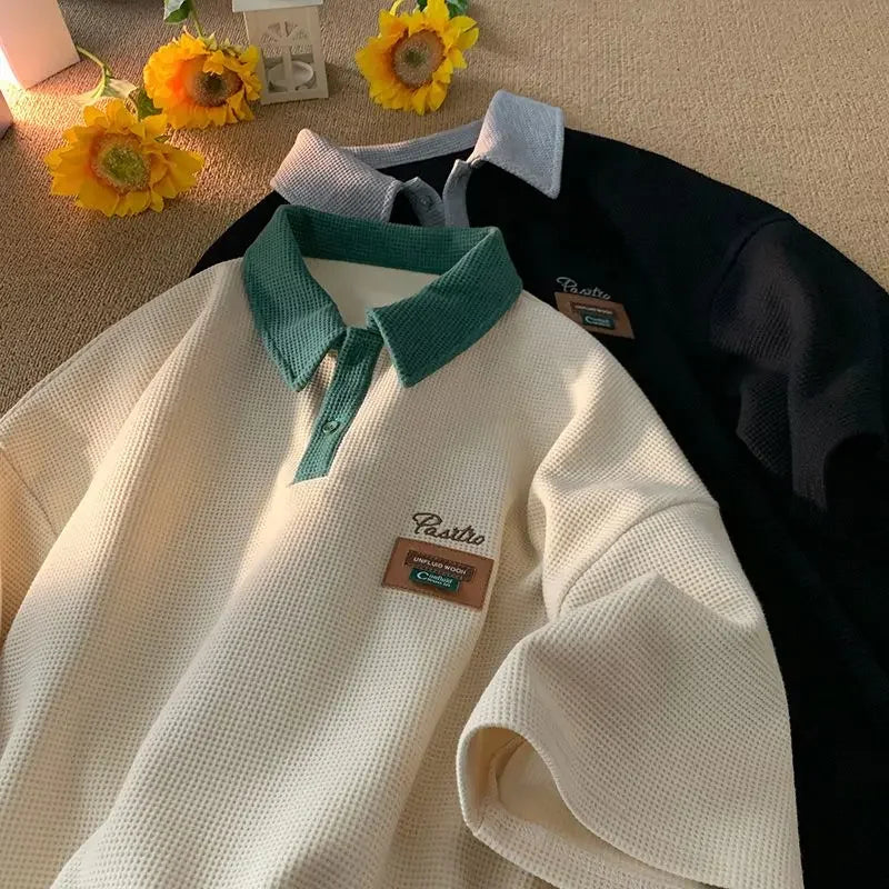 White polo shirt with a teal collar and a retro-style patch emblem.