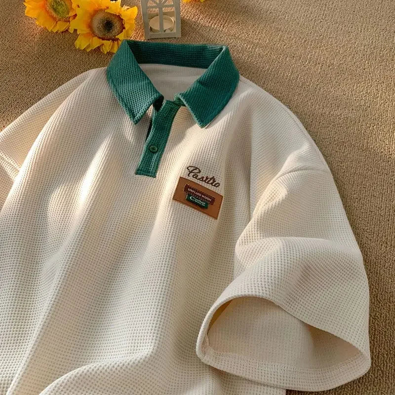 White polo shirt with a teal collar and a small patch emblem.